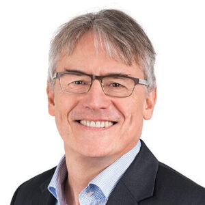 A man in glasses, short hair and a dress shirt and jacket smiles at the camera.