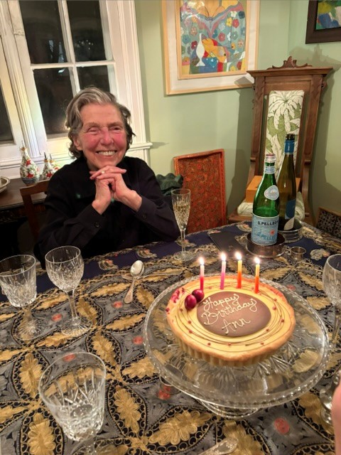Photo of Ann Laubstein sitting at a table smiling with a birthday cake that says, "Happy Birthday Ann".