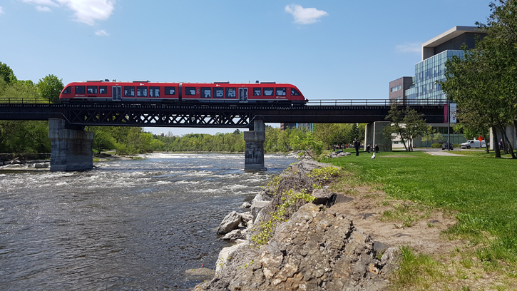 The O-Train crosses the bridge over the Rideau River from South Ottawa to Carleton on a sunny, summer day