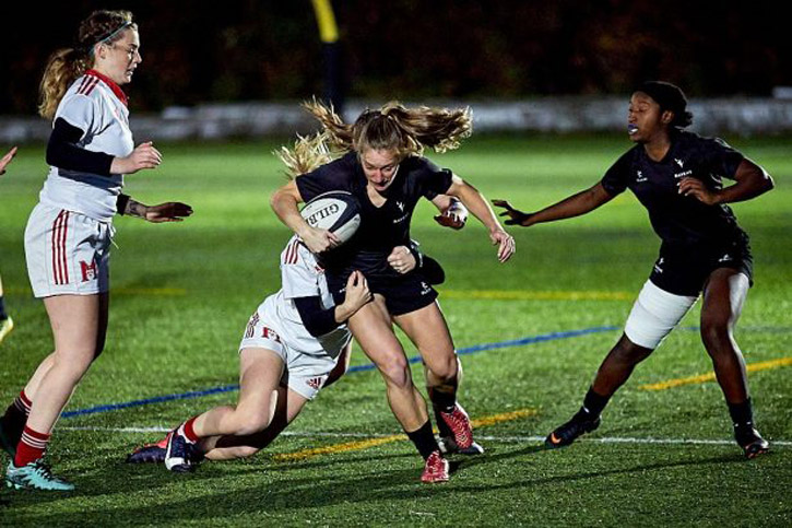 A Ravens women's rugby player tries to break a tackle from an opposing team member while she possesses the ball.