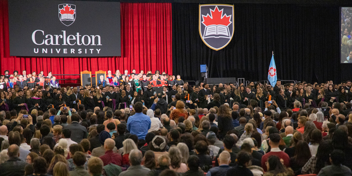 A view of Carleton's Convocation Ceremony, with a long line of graduating students turning to clap for their family and friends who are seated behind them.