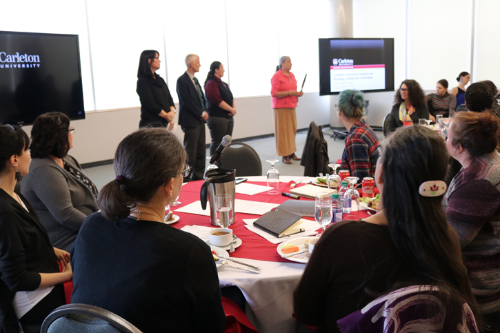 A group of people speak in a conference room while an audience listens during on-campus consultation conducted by the  Carleton University Indigenous Strategic Initiatives Committee (CUISIC) 