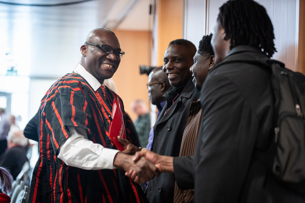 A man dressed in academic regalia shakes hands with students.