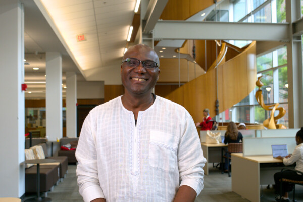Carleton University President standing and smiling in the library before delivering a recorded message, wearing a white shirt.