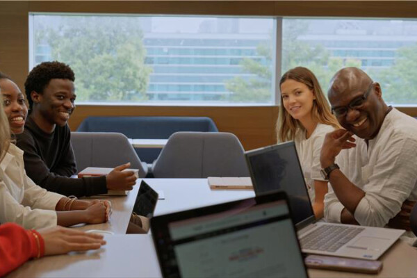 A group of people sitting at table with laptops while laughing together.