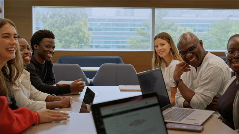 A group of people sitting at table with laptops while laughing together.