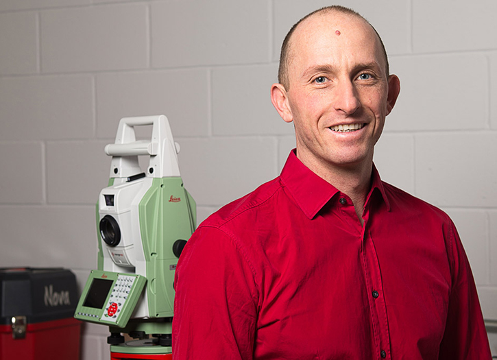 Stephan Gruber smiles at the camera while in a lab setting, with a piece of technical equipment behind him