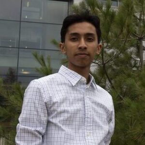 Sami is standing by a tree has, brown short hair and a black and white checkered shirt.