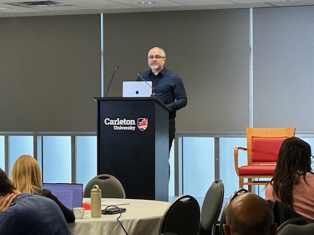 Damien Lee in a dark blue shirt presenting at a podium