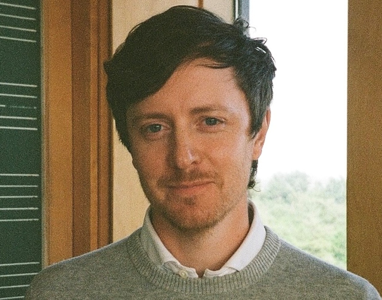 Man wit short, wispy brown hair, grey sweater and white button down shirt. 