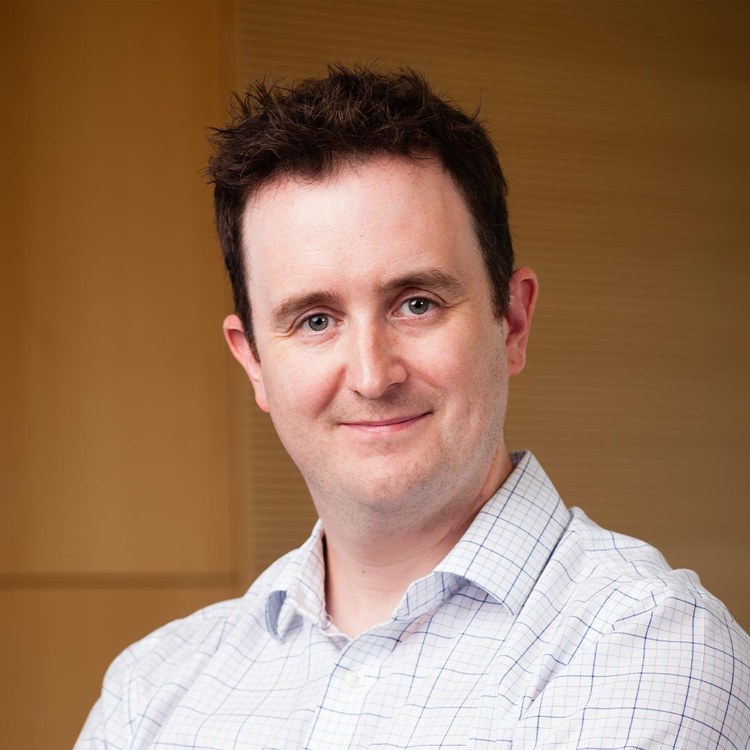 Dark haired man, smiling with checkered blue and white shirt. 