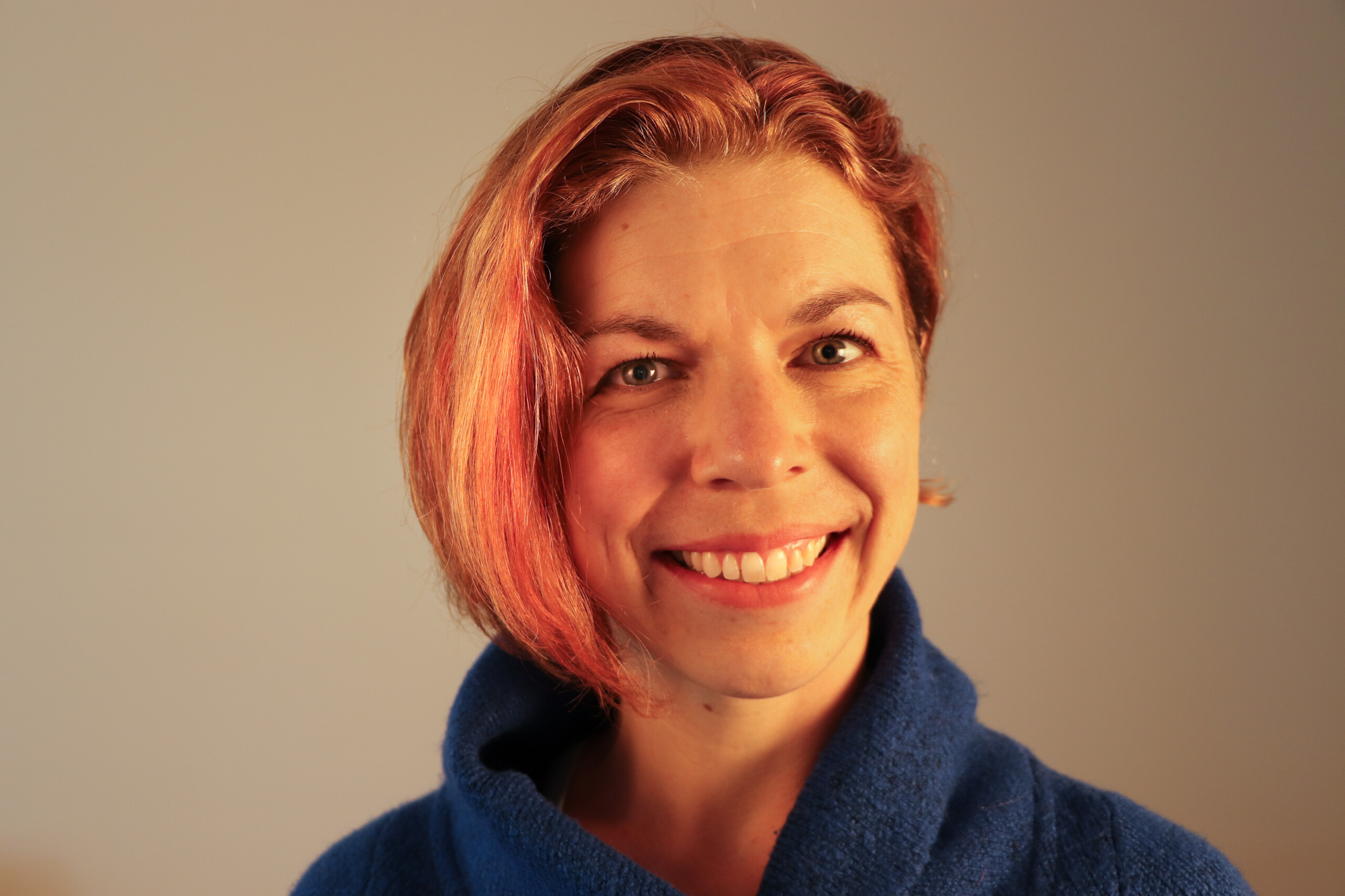 Woman wih red hear and dark blue sweater smiling. 