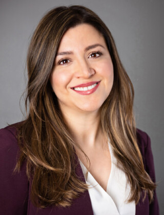 Smiling woman with long brown hair wearing a purple blazer and white blouse. 