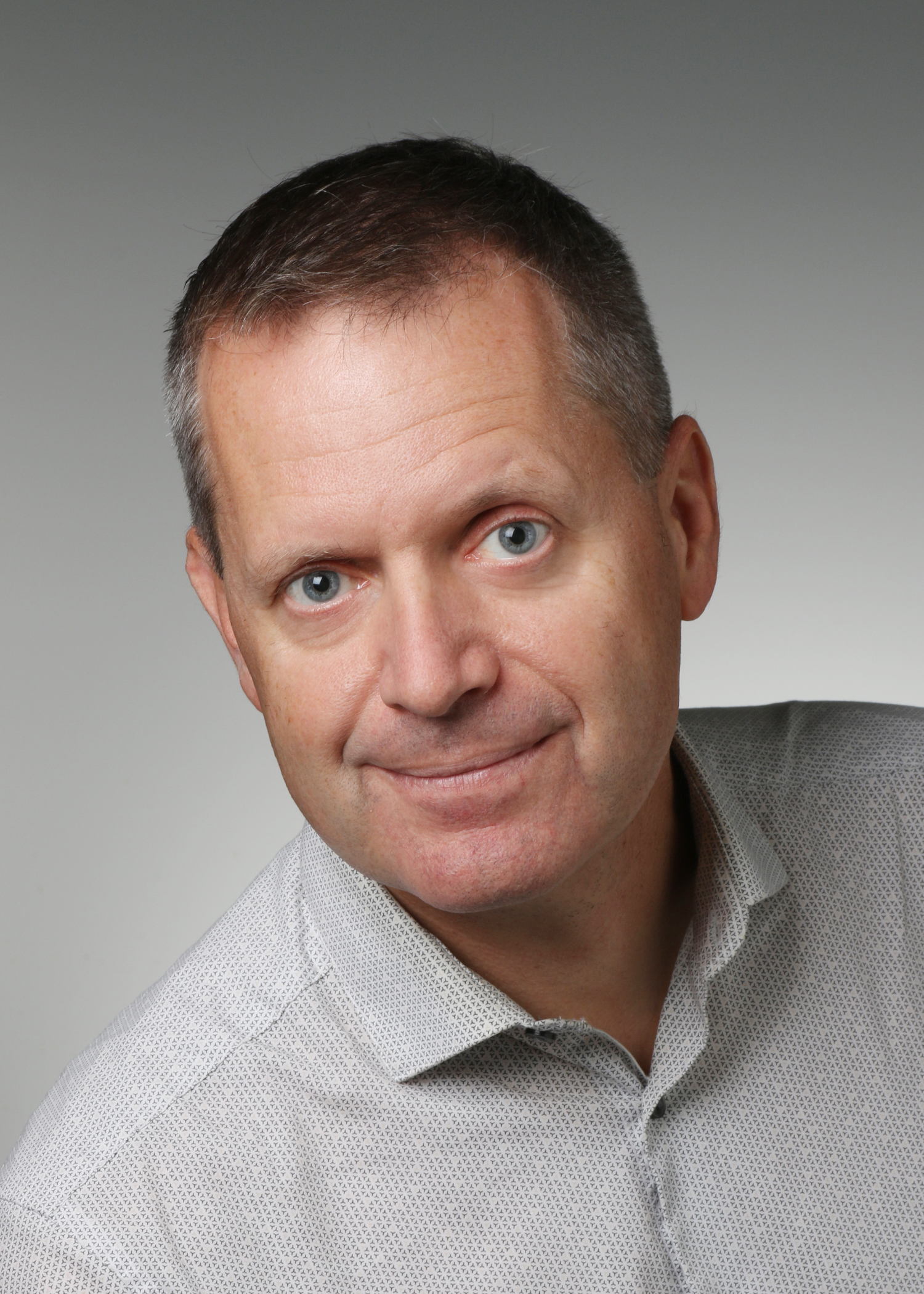 Older gentleman with sandy brown hair and blue eyes, wearing a grey gold shirtl. 