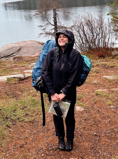 Woman in black slicker standing in the rain outside in the forest with a map, bag and tent. 
