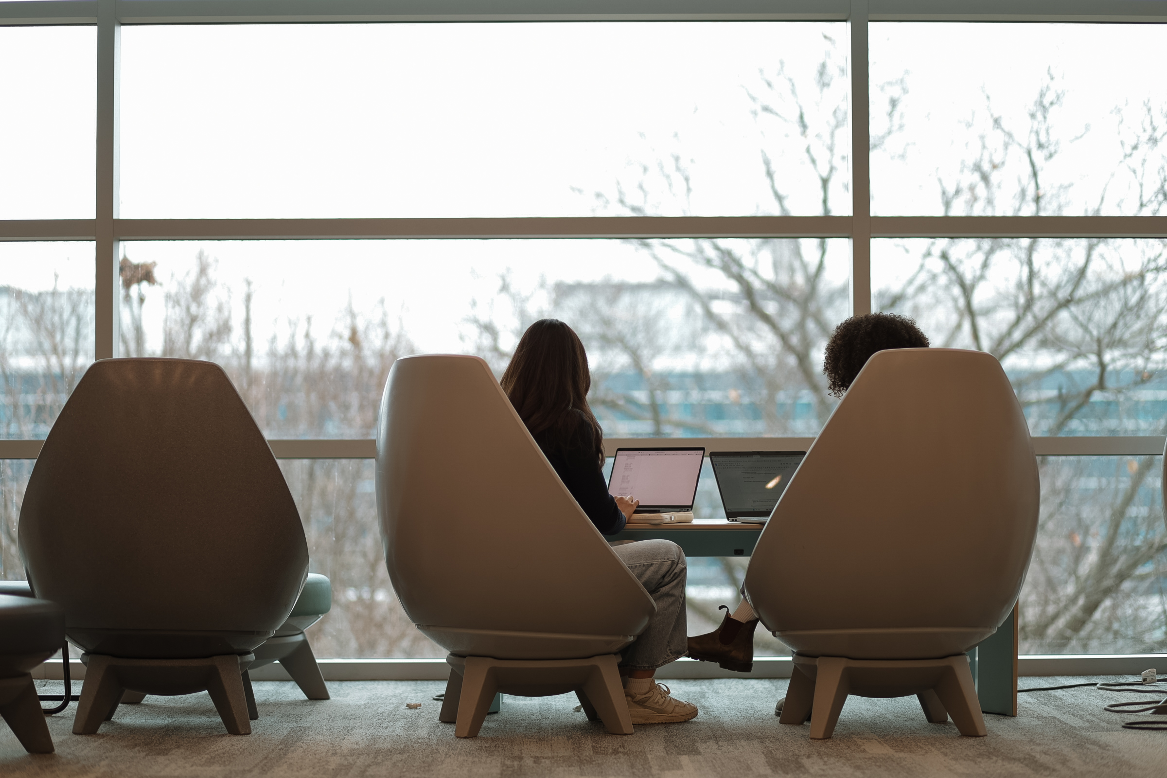 Two students sitting in lounge chairs looking out the window.