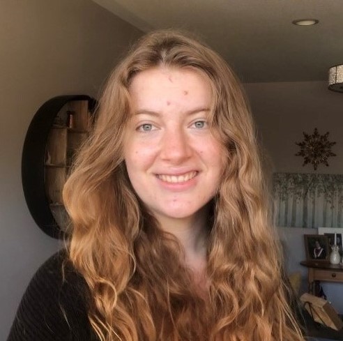 Red long, curly hair, wearing a black top.