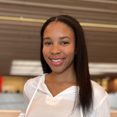 Shadea Nance (she/her) - Black woman with black long hair, smiling with red lipstick wearing a white top
