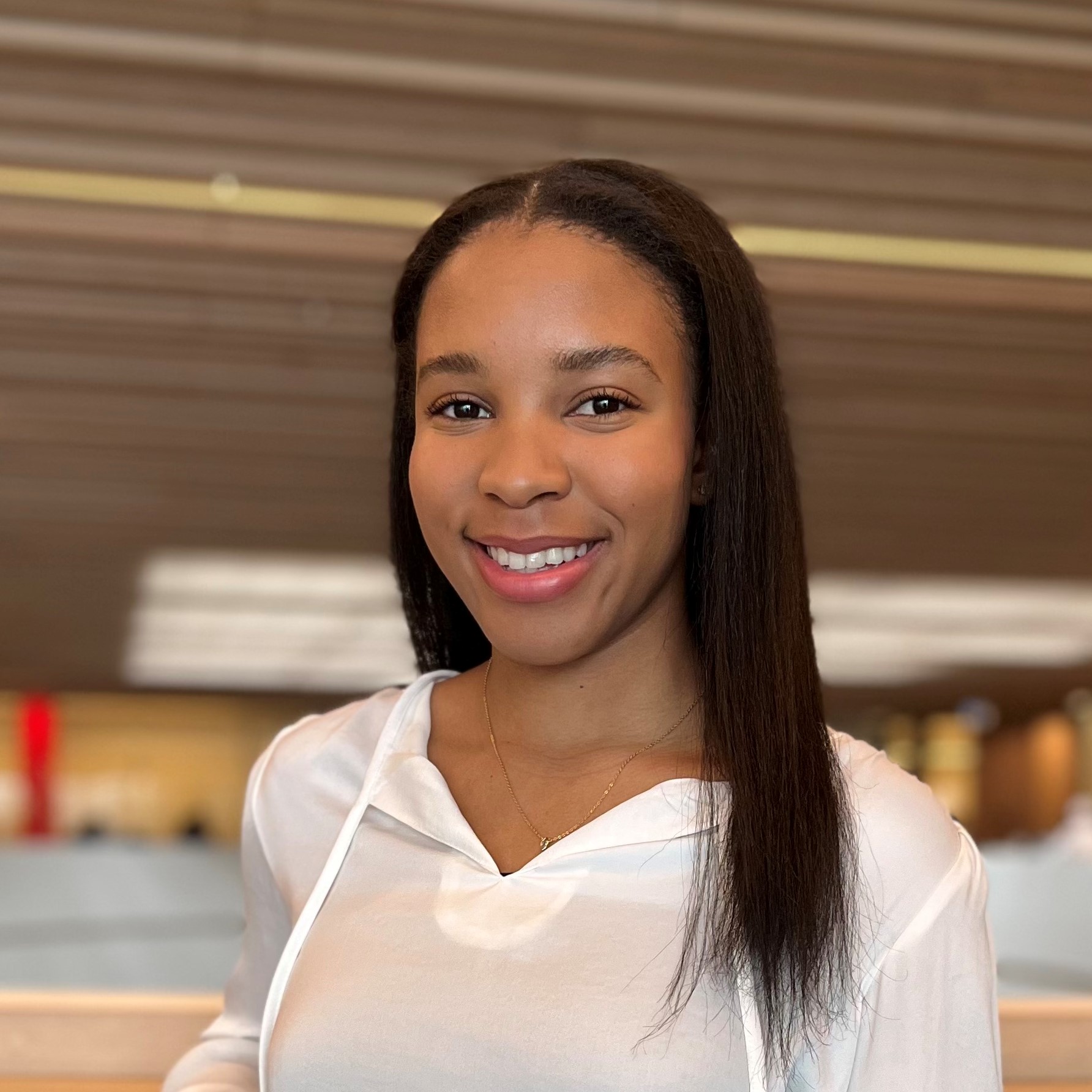 Shadea has long black straight hair and is wearing a white v-neck top.