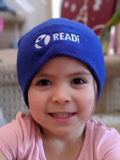 A smiling child wears a blue beanie with the READi logo