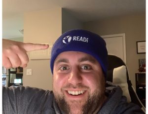 Ary is smiling at the camera and pointing to his blue tuque, with the READi logo