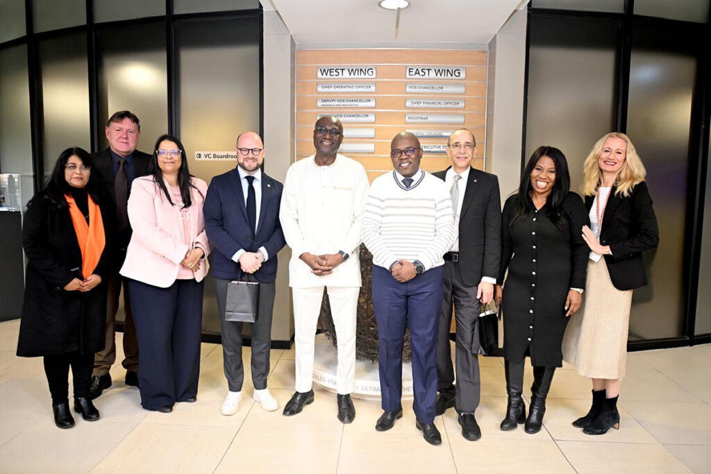 9 officials from Carleton and the University of Johannesburg pose for a group photo in the lobby of an academic building.