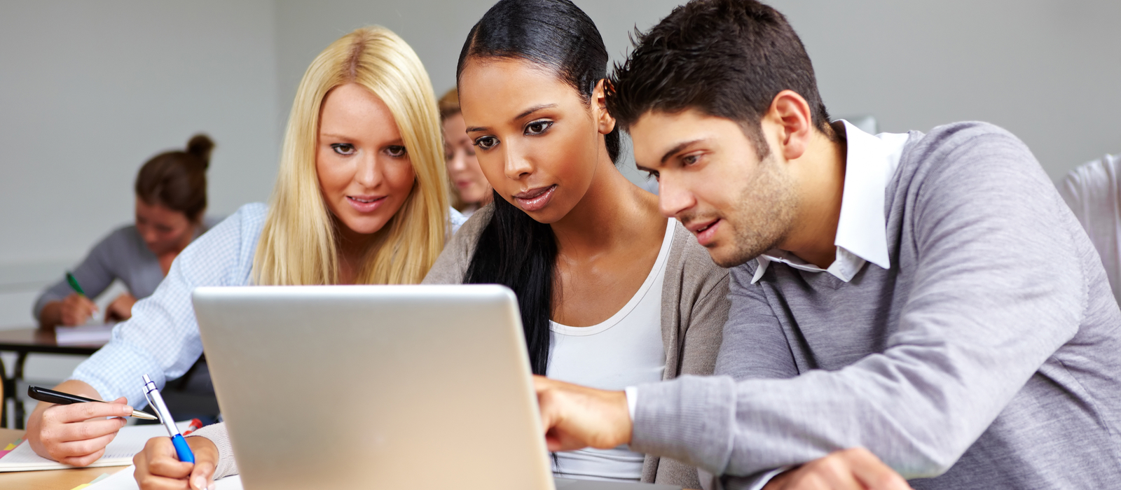 three students - a white woman, a black woman, and a white man - work on a computing problem as a team