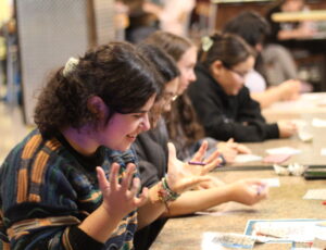 Student playing bingo from their table. Raised hands in exasperation as they wait for their number to be called.