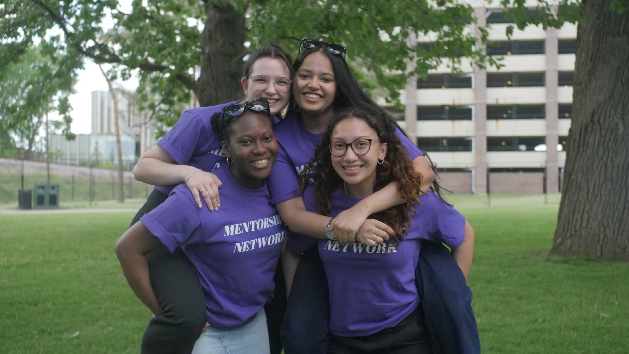 Four smiling First Year Connections Mentors wearing purple shirts outside.