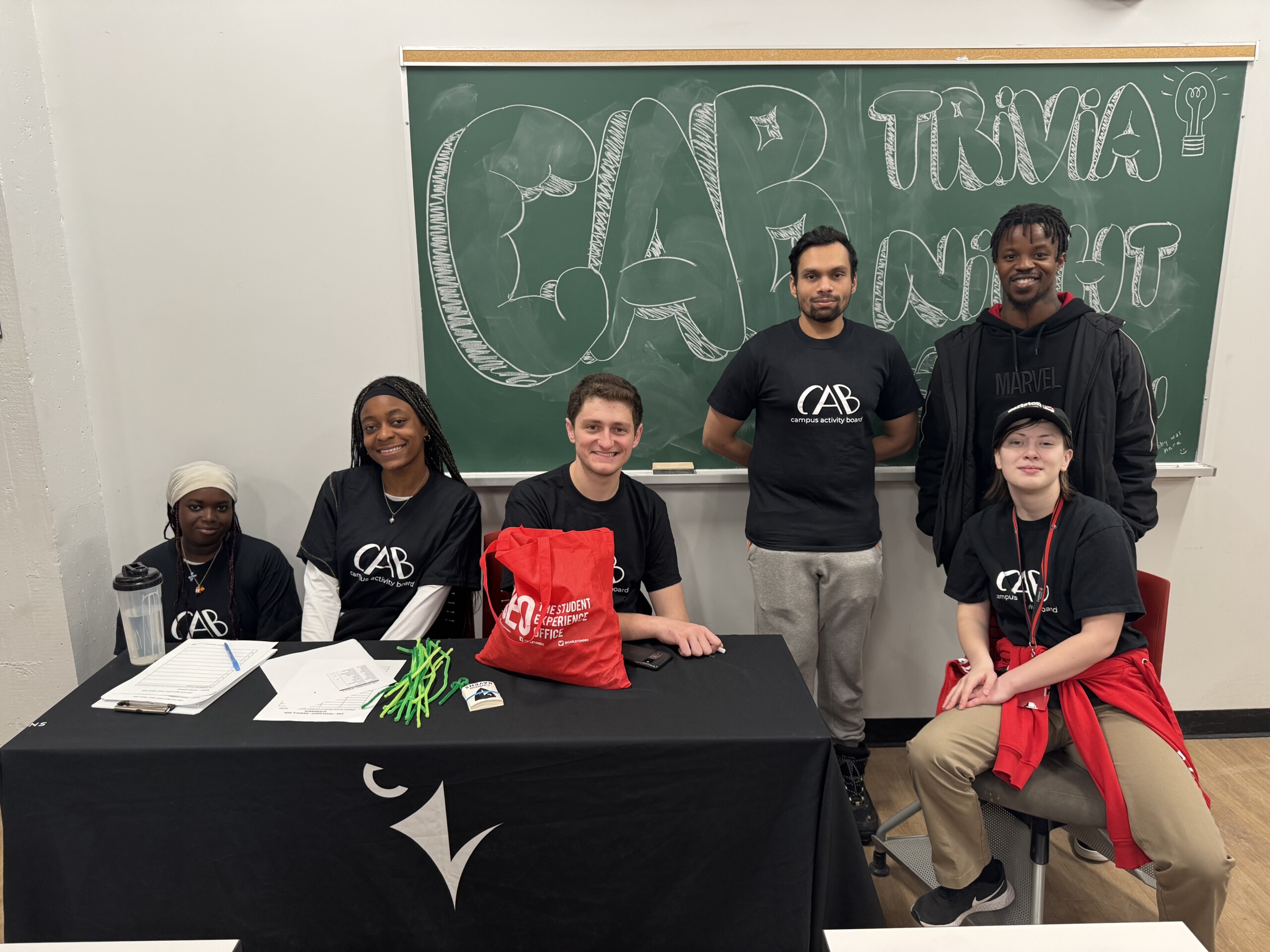 CAB Volunteers posing for group photo in front of chalk board that says TRIVIA NIGHT.