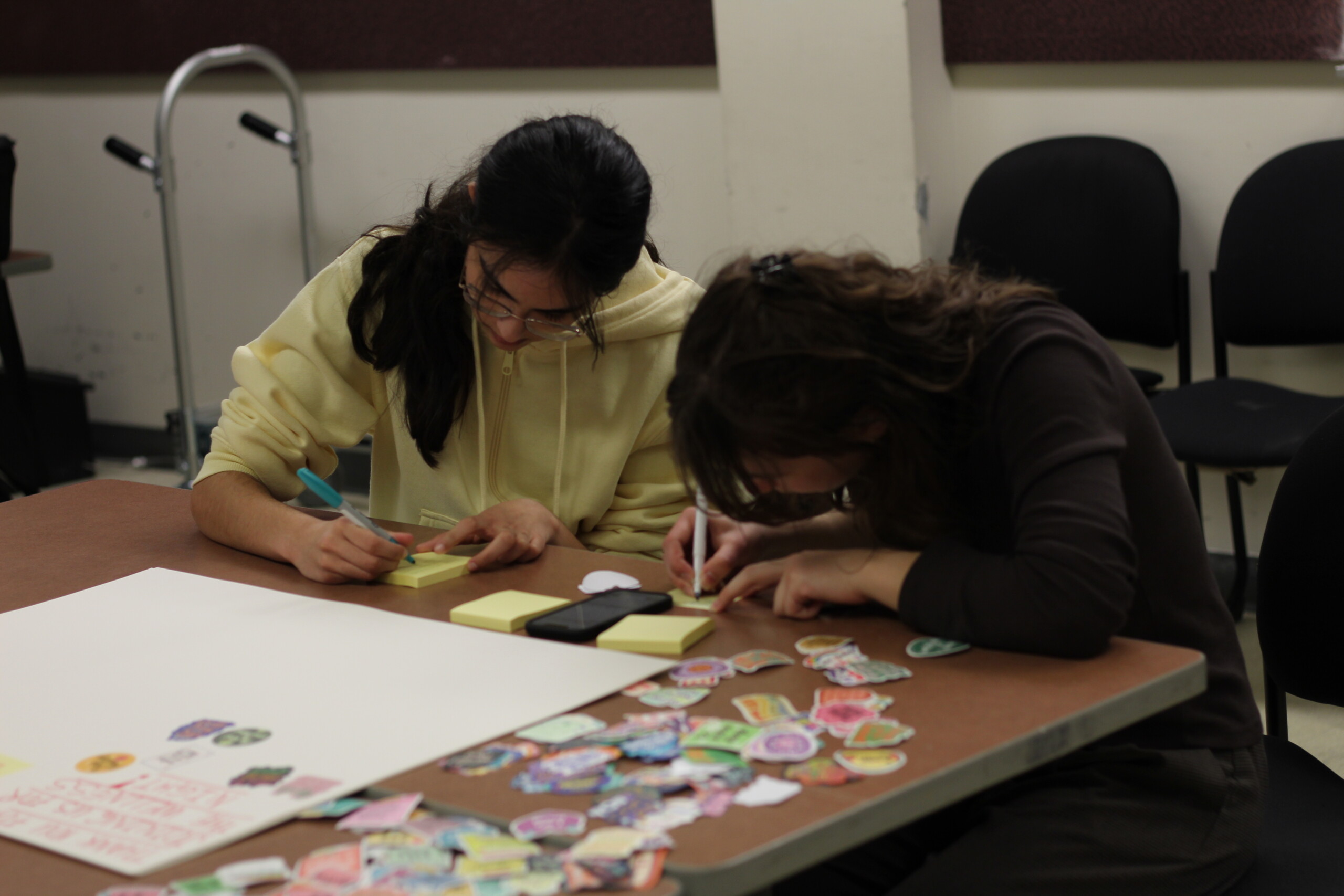 Two students writing on a poster on their table together.