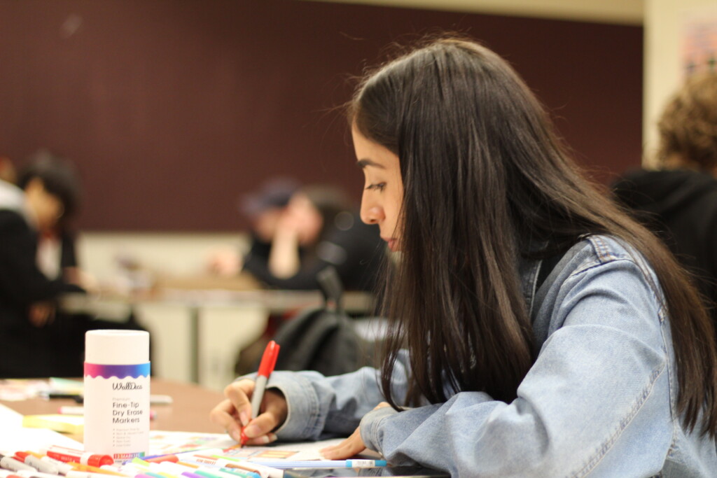 Student reflecting on their work as the write at a desk.
