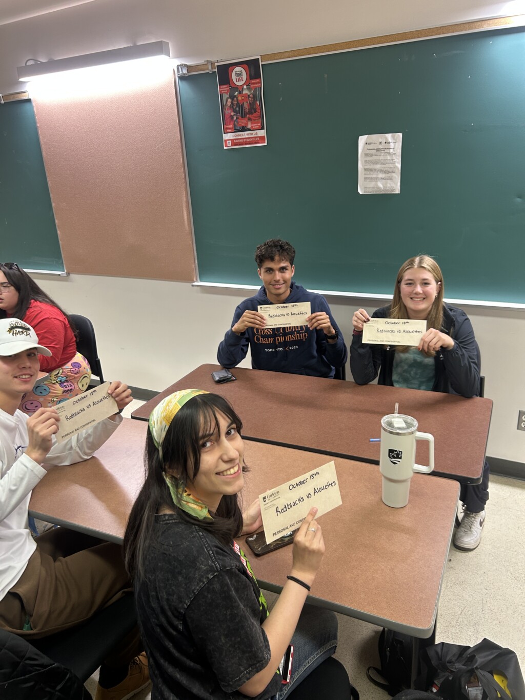 Students sitting at a desk and displaying their winning envelopes.