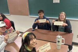 Students sitting at a desk and displaying their winning envelopes.