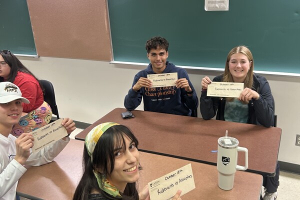 Students sitting at a desk and displaying their winning envelopes.