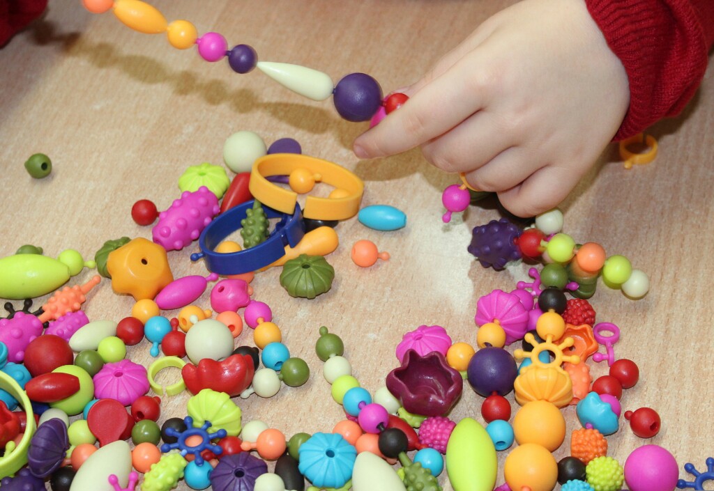 Close up photo of a student making crafts with beads.