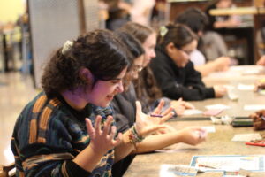 Student playing bingo from their table. Raised hands in exasperation as they wait for their number to be called.