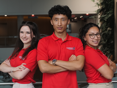 Three students wearing Carleton Red Polos. Smiling and posing for group photo while crossing their arms.