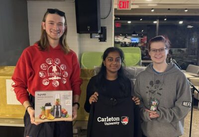 Three students showing off their raffle prizes after karaoke: Personal Blender, Ravens sweater, a miniature gum ball machine.