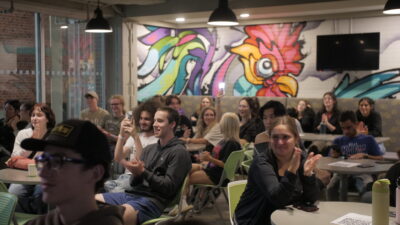 Large group of students cheering for karaoke performers from their seats.