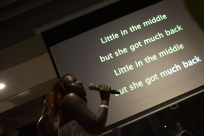 Student singing with microcu_people_phone with karaoke lyrics on screen behind them.
