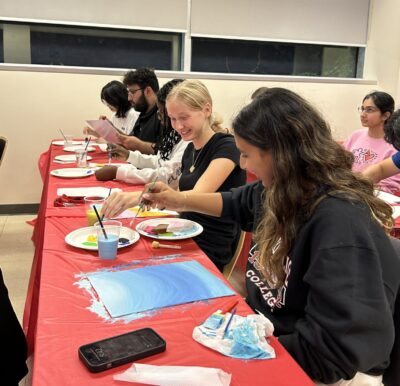 Students sitting in a row and working on their canvases.
