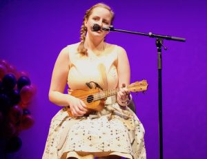 Emma glances at the audience while playing her ukulele.