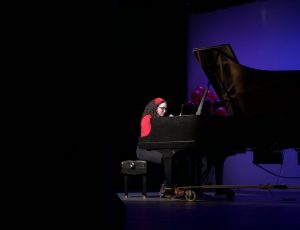 Gabrielle dressed in red and black sits at the grand piano.