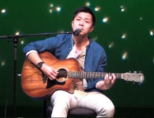 Yang Na playing his guitar on the stage with a green background with stars