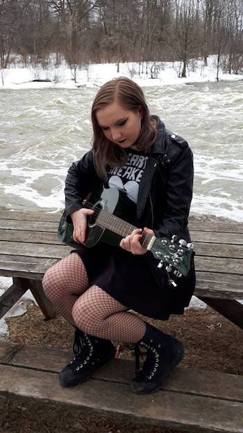 Emily playing her guitar beside the river