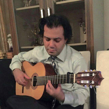 Hooman in a tie seated playing his acoustic guitar