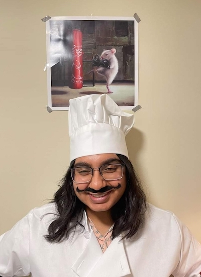 Lucksiha dressed as a chef with a poster on the wall above her showing Remy, the rat from the movie Ratatouille