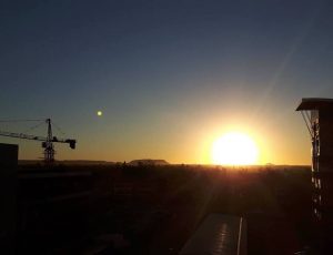 View from a rooftop terrace over a city. A construction crane against the sunset.
