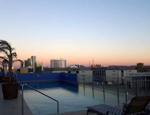 Rooftop swimming pool with sunset over the city in the background.